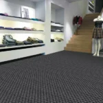 Dark grey grid-patterned fireproof carpet in a modern retail clothing store.